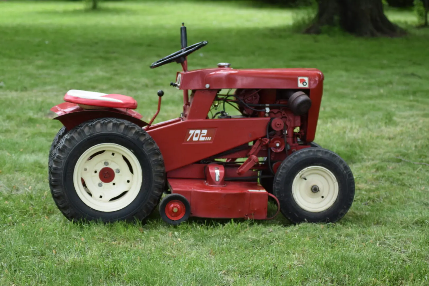 A red tractor sitting in the grass next to some trees.