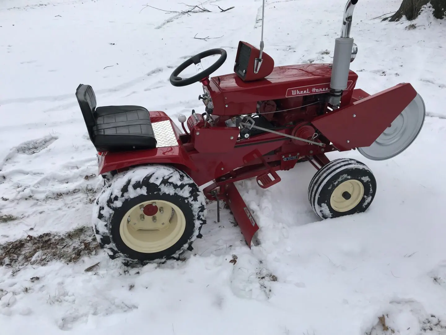 A red tractor is in the snow with a plow.
