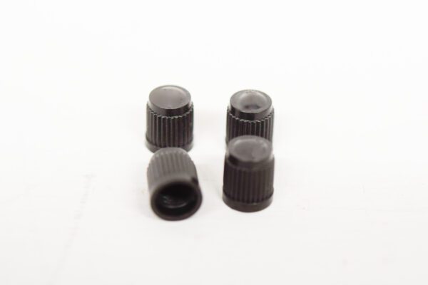 Four black plastic knobs on a white surface, resembling (4) Black Tire Valve Stem Caps.