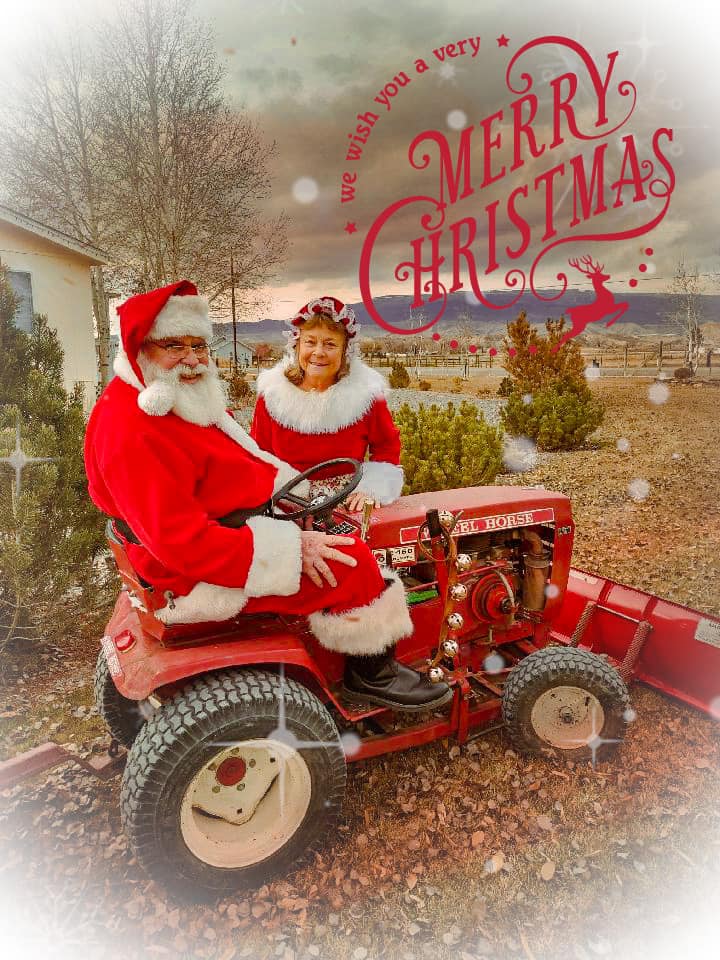 A man and woman dressed as santa claus riding on a red tractor.